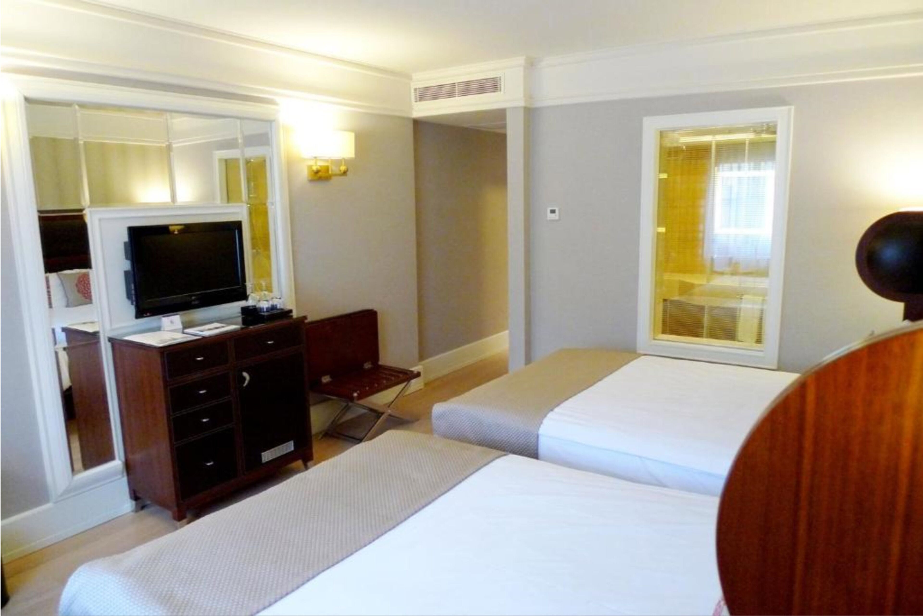 A hotel room with two beds, a TV, a desk, and a mirror.