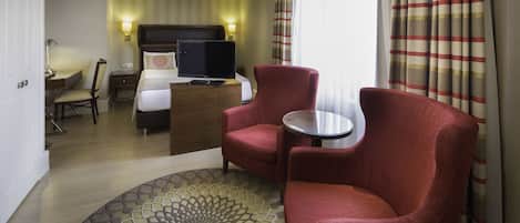 A hotel room with a bed, a desk, two armchairs, a small table, and a patterned rug.