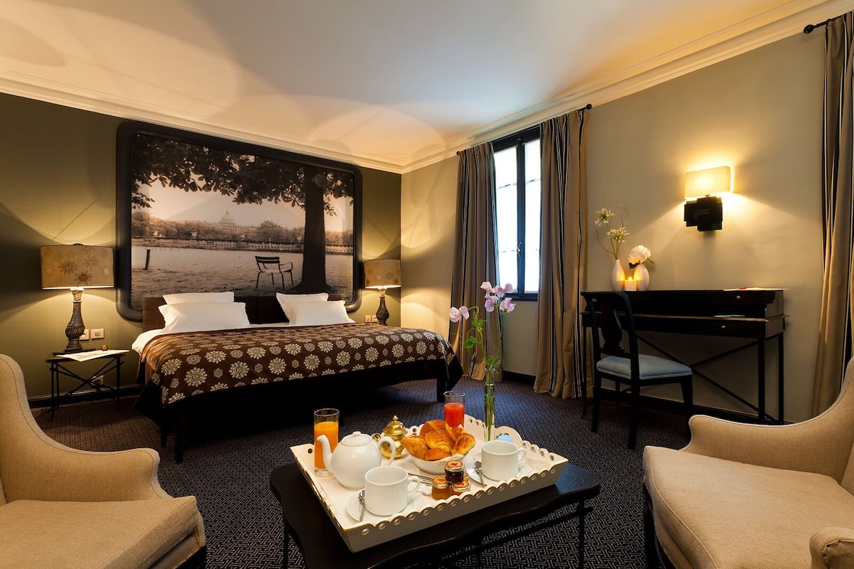 Hotelkamer met een bed, bureau, stoel, een salontafel met ontbijtartikelen en een groot raam met gordijnen.
