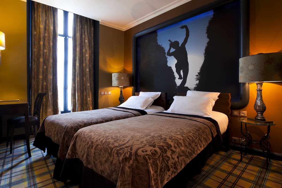 Een hotelkamer met twee bedden, een groot muurschilderij, een bureau en een stoel.