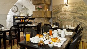 Un ambiente para desayunar con mesas preparadas para comer, un reloj en la pared y una pared de piedra con un mural.