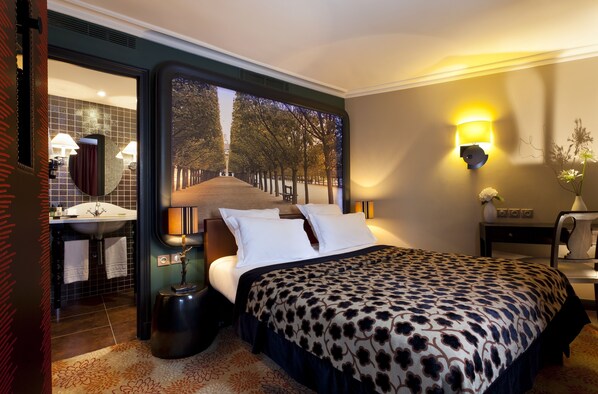 A hotel room with a large bed, a bathroom with a sink and mirror, and a view of trees through a window. - Les Fontaines du Luxembourg (Paris)