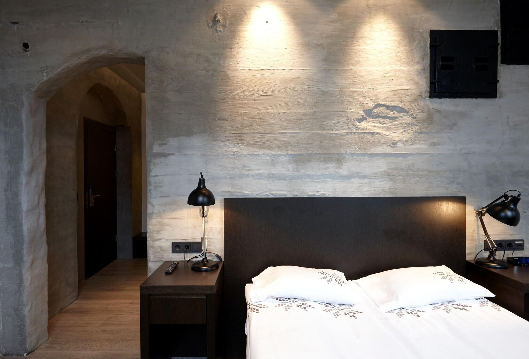 Un dormitorio con cama, dos mesitas de noche con lámparas, suelo de madera y pared de piedra.