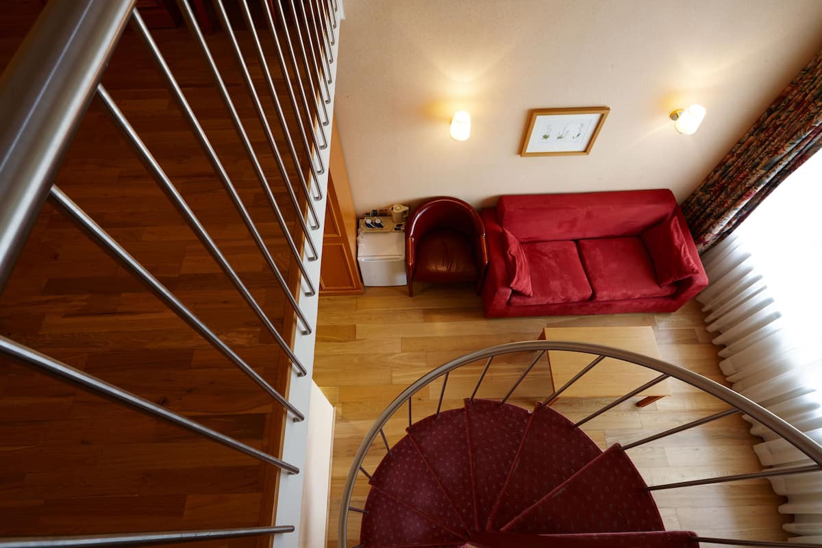 Eine Treppe mit einem rot gepolsterten Stuhl und einer roten Couch in einem Raum mit Holzböden und einem weißen Heizkörper.