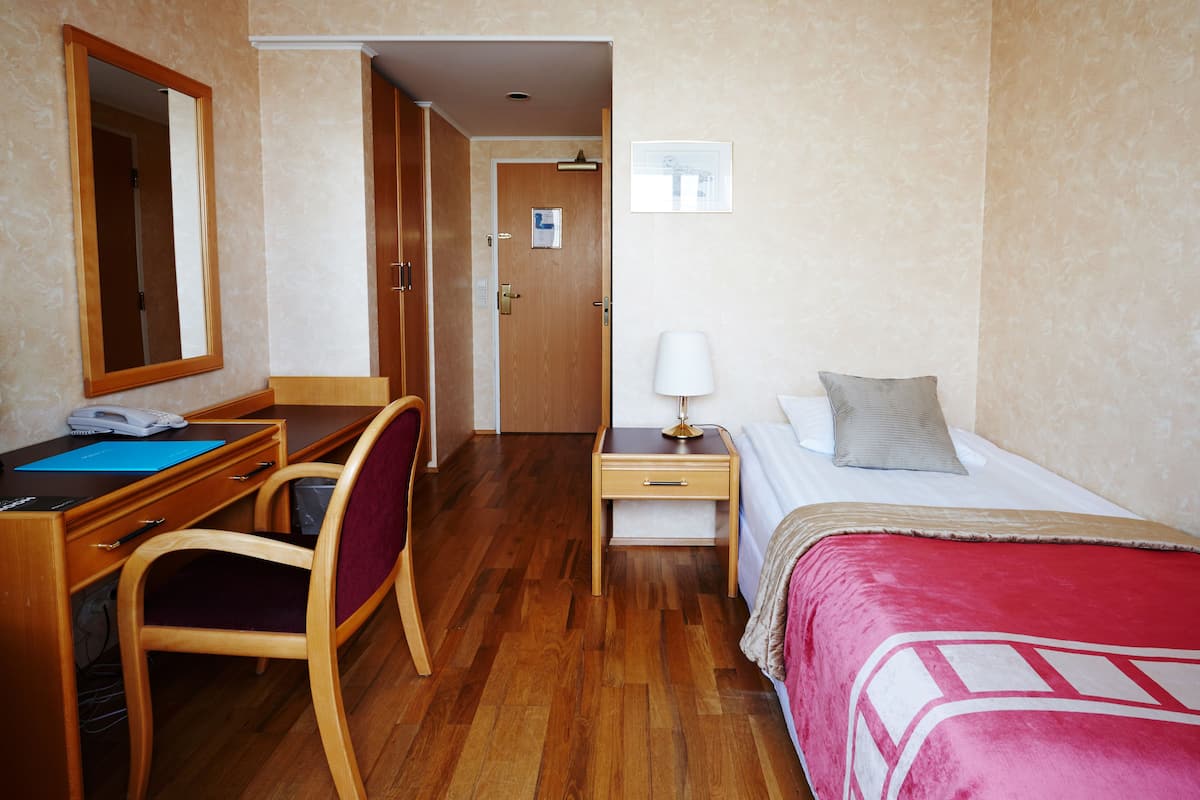 Ein Hotelzimmer mit einem hölzernen Schreibtisch, einem Stuhl und einem Bett mit roter Decke.