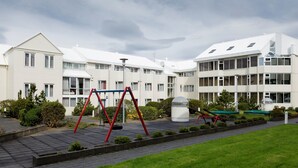 Edificio residencial con un parque infantil al frente, que incluye columpios y un tobogán.