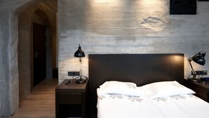 Habitación de hotel con cama, dos mesitas de noche, una lámpara y un aplique de pared.