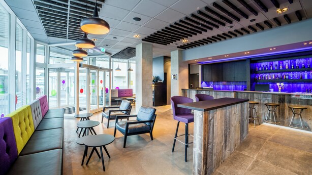 Un área de bar moderna con mostrador de madera, asientos morados y vistas a la ciudad a través de amplios ventanales.