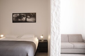 A bedroom with a bed, bedside lamps, a nightstand, a sofa, and a framed picture on the wall.
