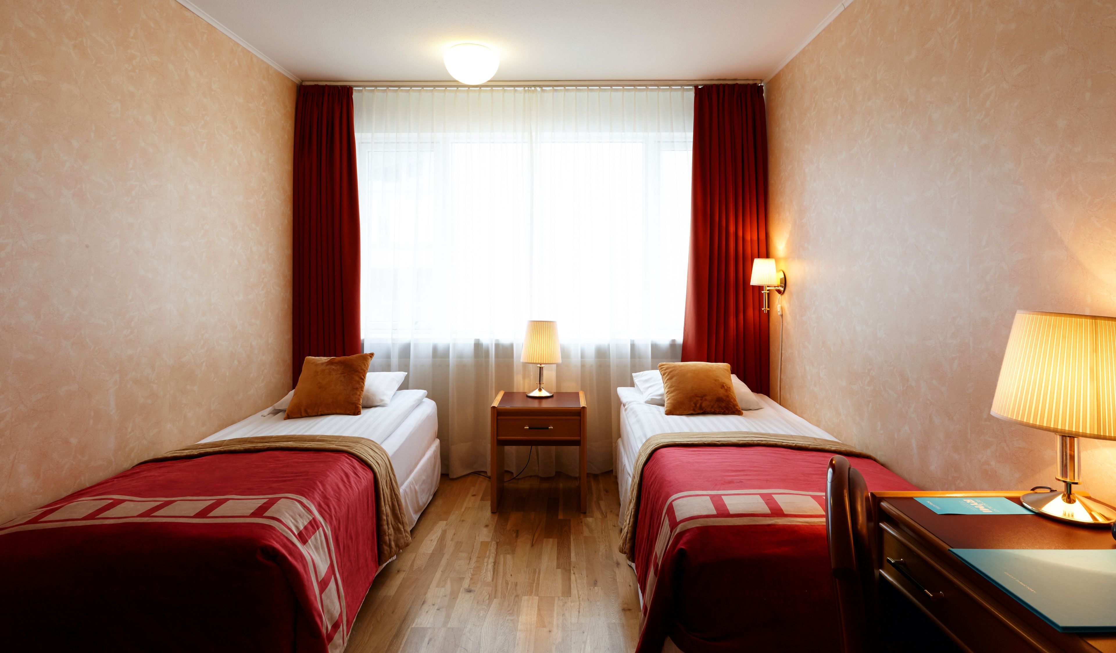 A hotel room with two beds, a nightstand, a desk, and a lamp.