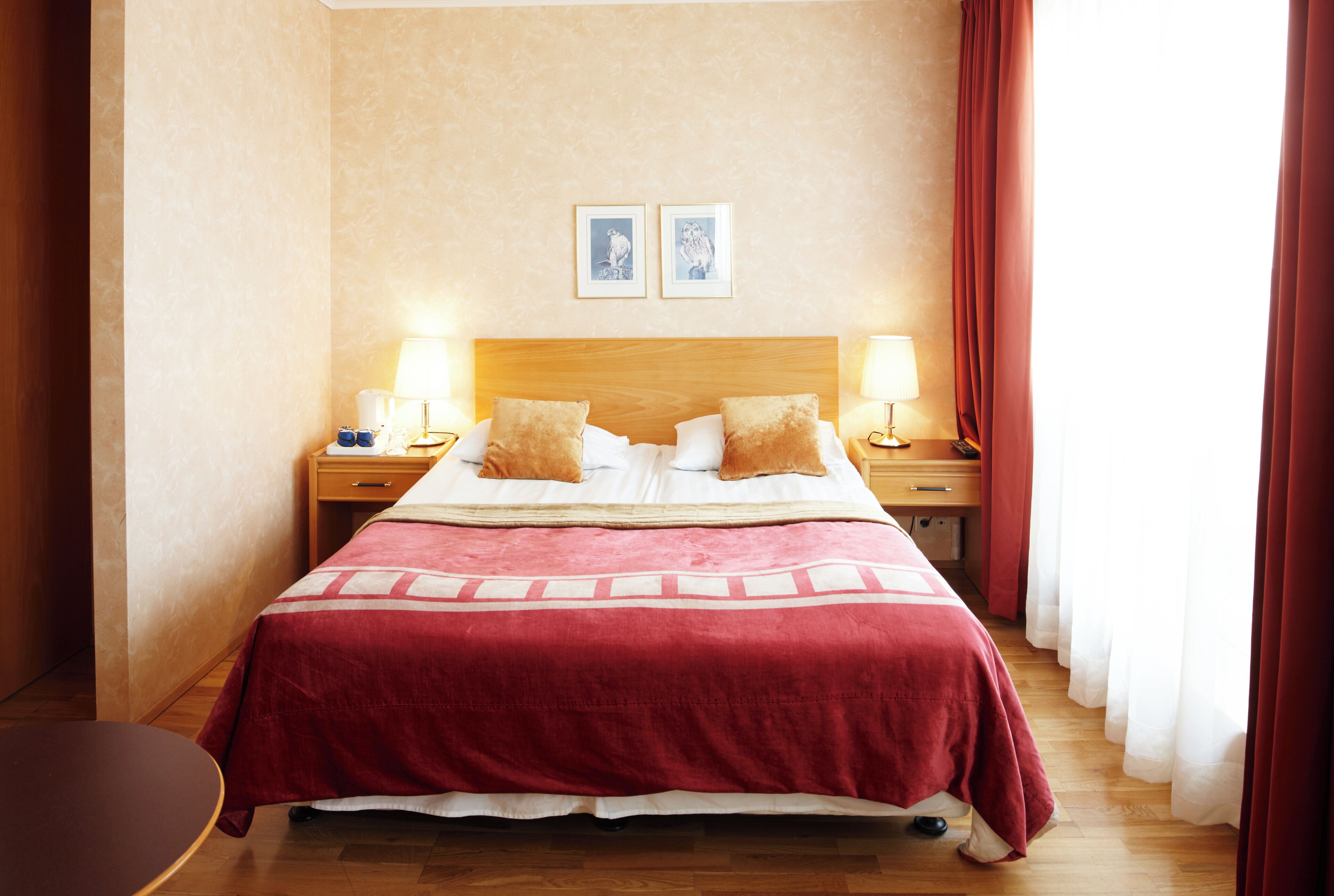 Una habitación de hotel con una cama grande, dos mesitas de noche con lámparas, un cabecero de madera y dos cuadros enmarcados en la pared.