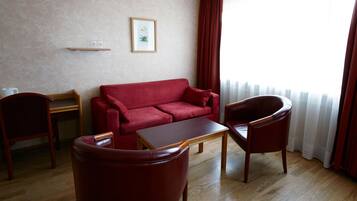 A red sofa, a wooden coffee table, and two leather armchairs in a room with wooden flooring and a beige wall.