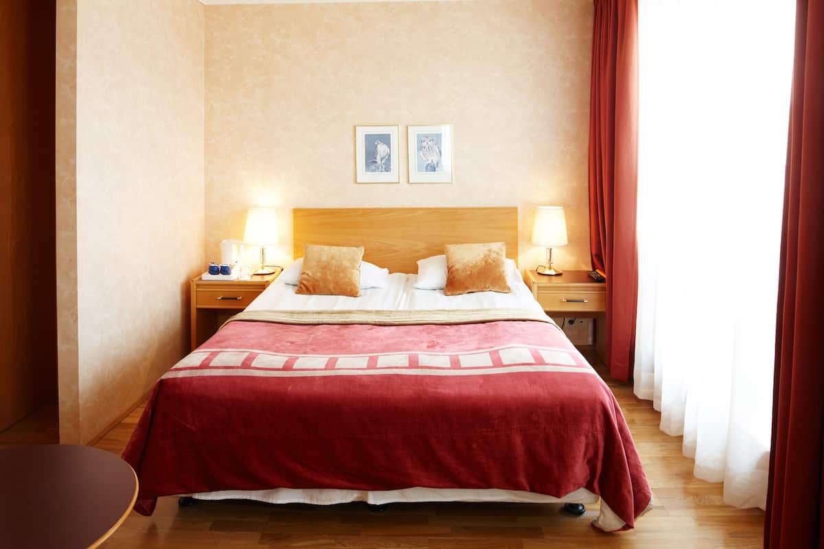 Ein Hotelzimmer mit einem großen Bett, zwei Nachttischen mit Lampen, einem hölzernen Kopfteil und zwei gerahmten Bildern an der Wand.