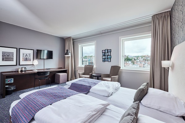 A hotel room with two beds, a desk, a chair, a TV, and a view of the city.