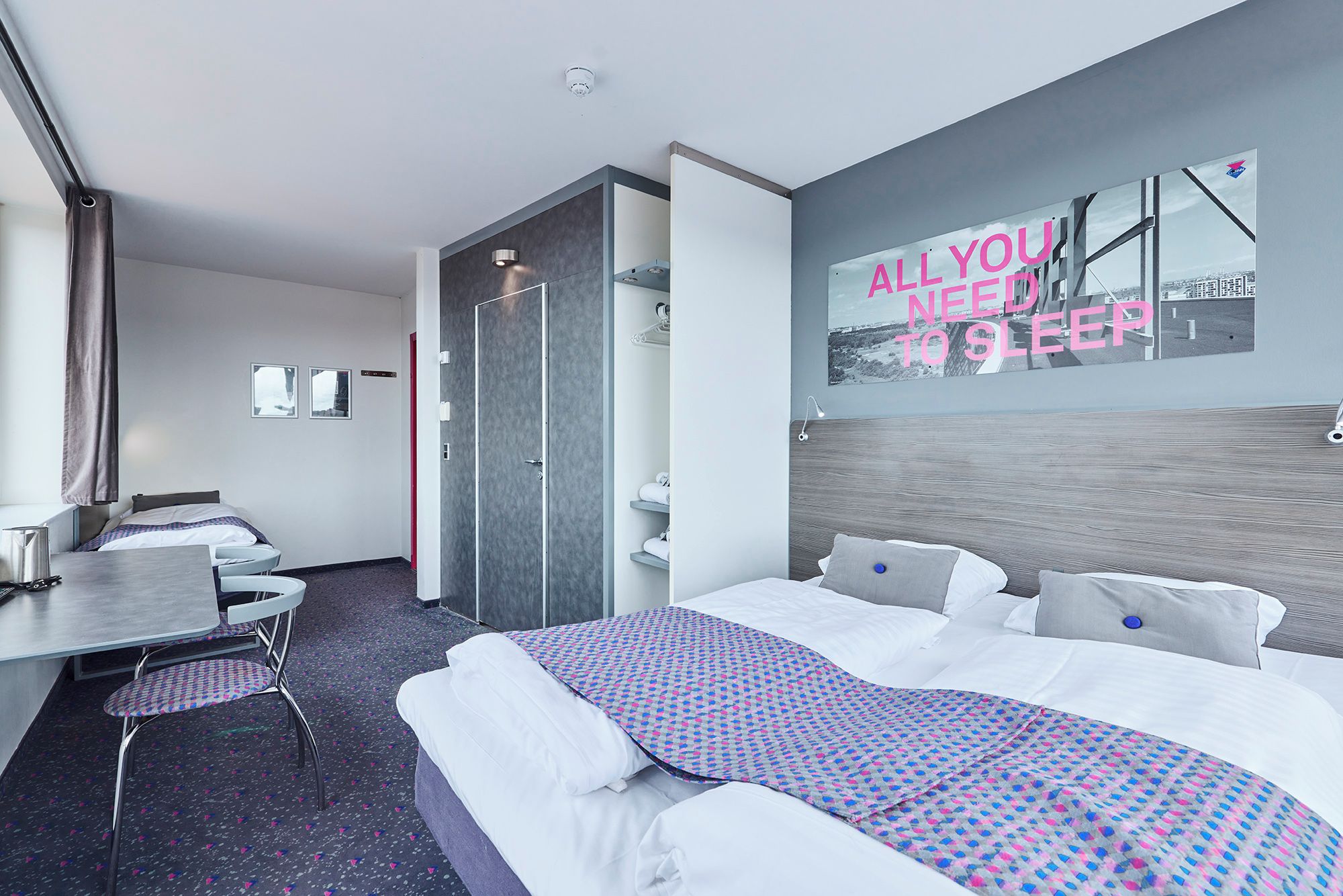A modern hotel room with a bed, a desk, and a bathroom.