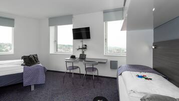 Habitación de hotel con dos camas, un escritorio con una computadora portátil, un televisor y una ventana con vista a la ciudad.