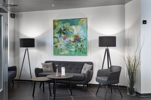 A modern waiting area with a grey sofa, two armchairs, a coffee table, and two floor lamps. A large abstract painting adorns the wall. - CABINN Vejle Hotel (Vejle)
