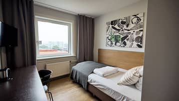 Une chambre d’hôtel comprenant un lit, un bureau, une chaise, un radiateur, une fenêtre avec des rideaux et une œuvre d’art accrochée au mur.