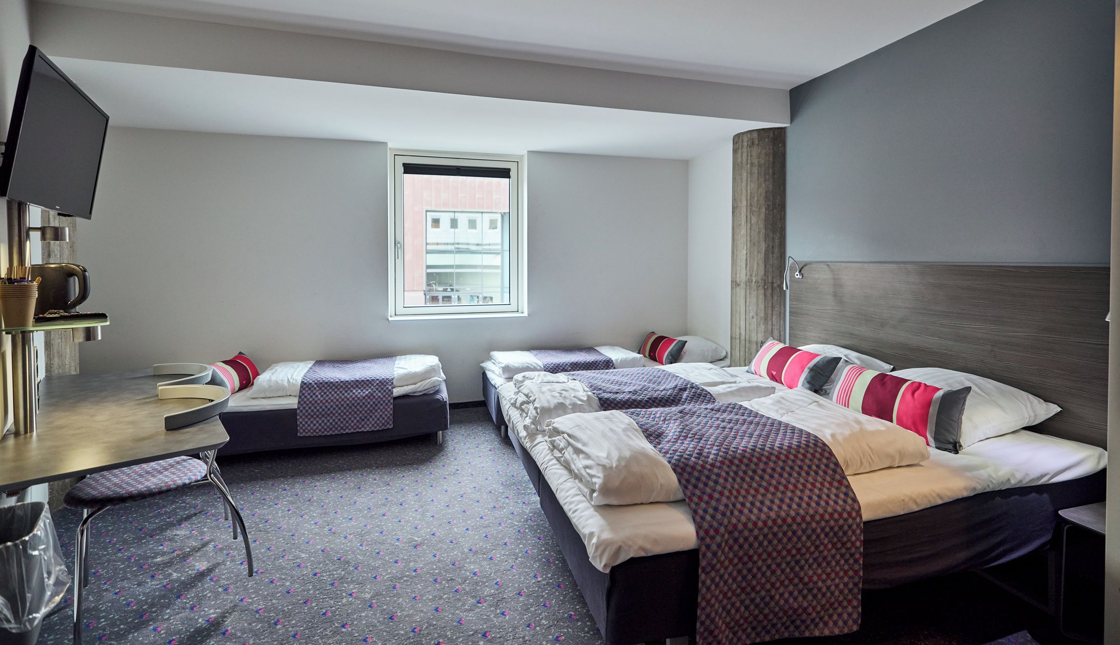 A hotel room with a bed, a desk, a chair, a TV, and a window.