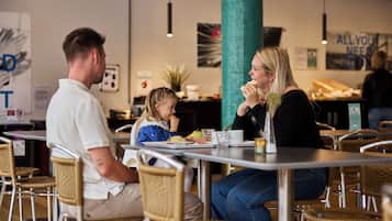 Een gezin geniet van een maaltijd in een modern café met rieten stoelen en een centrale pilaar.