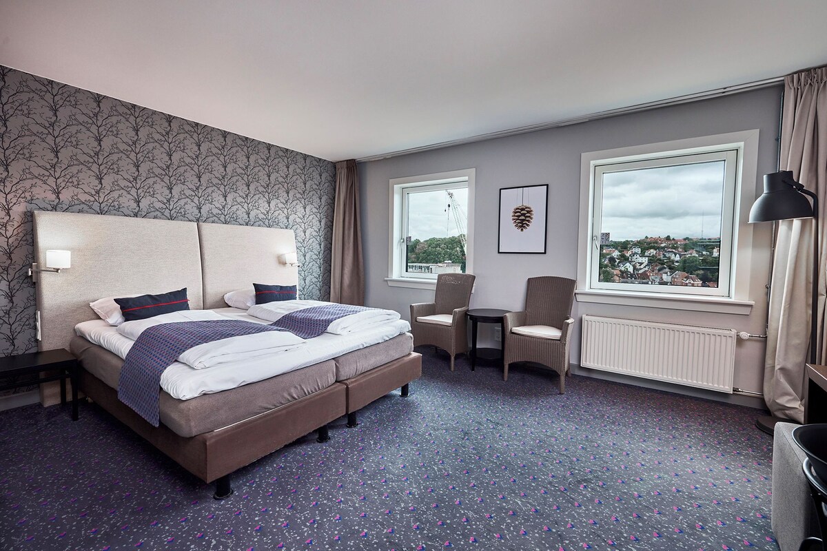 Habitación de hotel con cama, dos sillas, una mesa, ventana con vistas y un radiador.