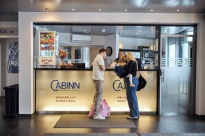 A hotel reception area with a counter, a snack bar, and a welcome sign. - CABINN Vejle Hotel (Vejle)