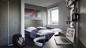 Une chambre d’hôtel moderne avec deux lits, un ordinateur portable sur le bureau et une fenêtre donnant sur un beau paysage.