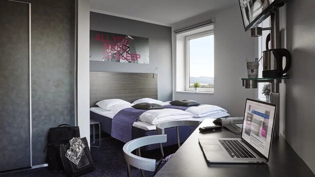 A modern hotel room with two beds, a laptop on the desk, and a window with a view.