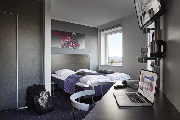 A modern hotel room with two beds, a laptop on the desk, and a window with a view. - CABINN Vejle Hotel (Vejle)