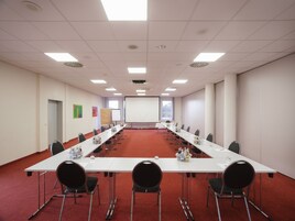 Un salón de conferencias con una larga mesa, sillas, una pantalla de proyector y una pizarra.