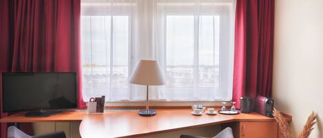A hotel room with a desk, two chairs, a TV, a lamp, a coffee maker, and a vase with dried plants.