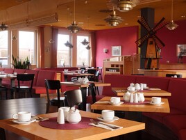 Een restaurant met rode bekleden zitbanken en houten tafels, met een windmolen decoratie aan de muur.