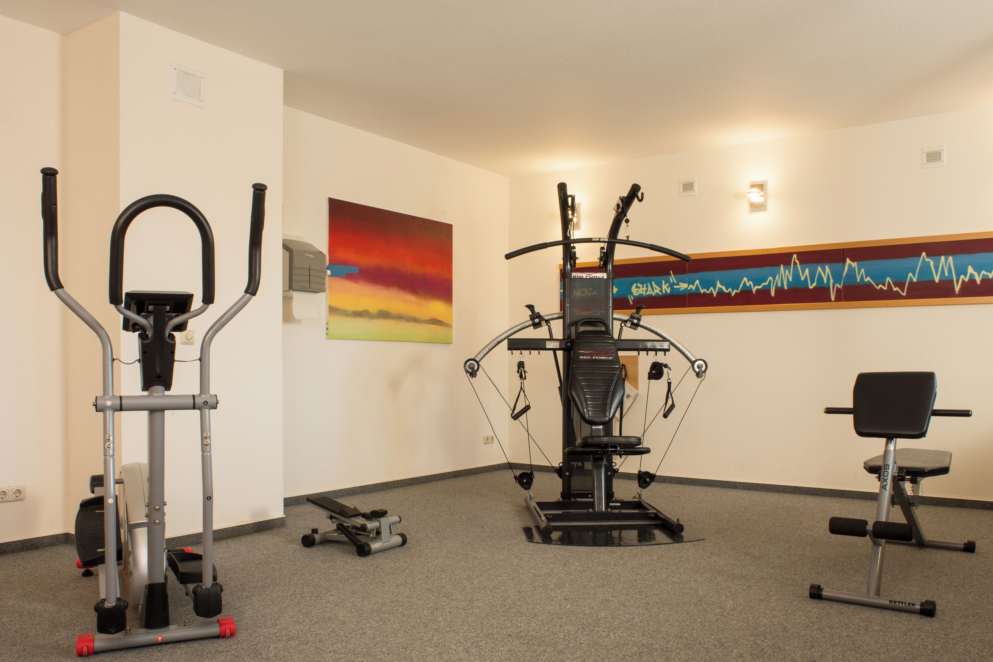 Ein Fitnessraum mit Trainingsgeräten, einem Gemälde und einer Wandanzeige.
