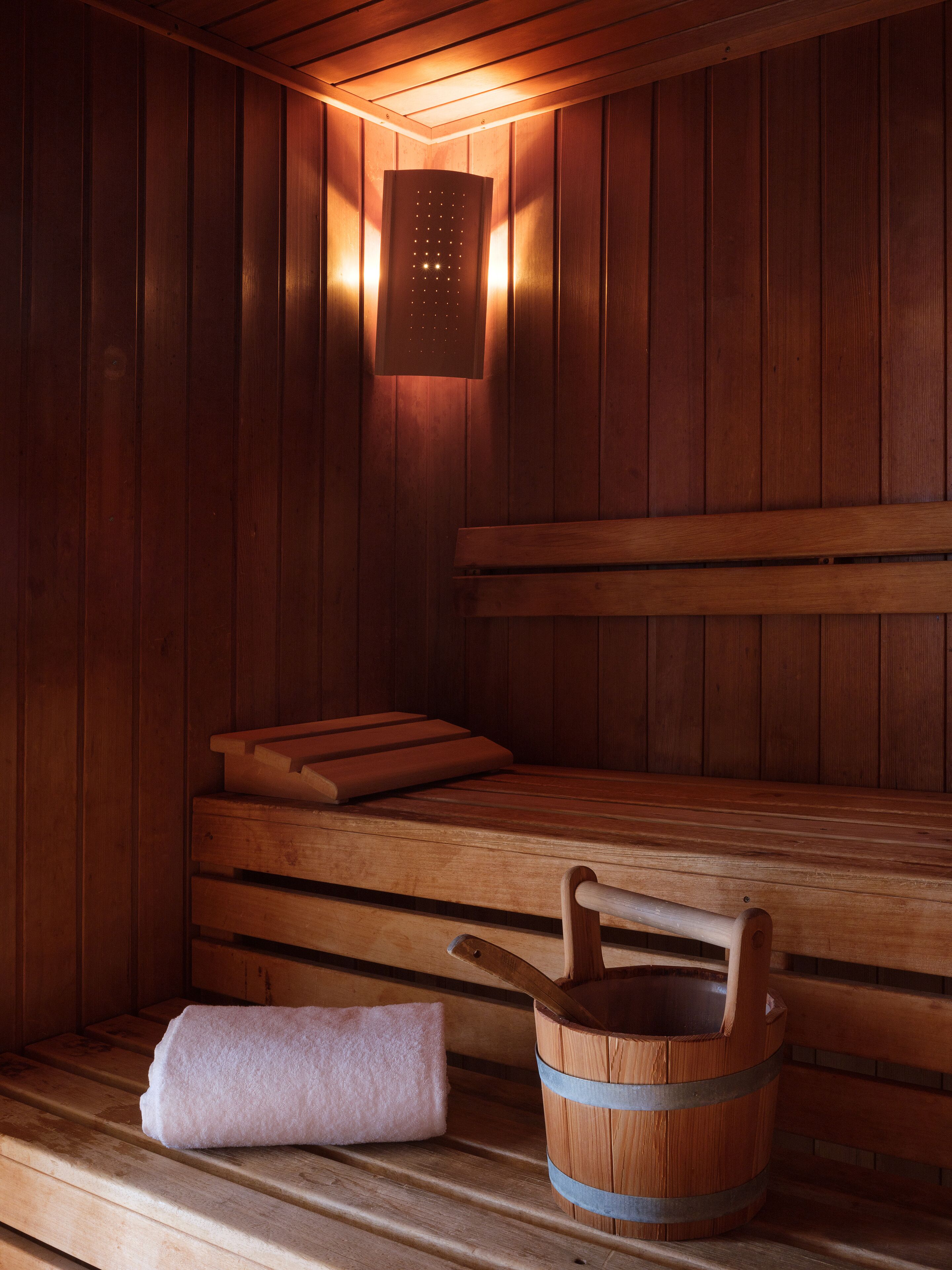 A wooden sauna with benches, a towel, and a wooden bucket.