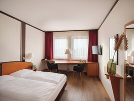 Habitación de hotel con cama, escritorio, silla y televisión.