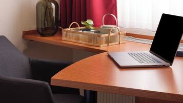 Ein Laptop auf einem Holztisch zusammen mit einer Vase mit getrocknetem Pampasgras, einem gewebten Korb und einer Lampe.