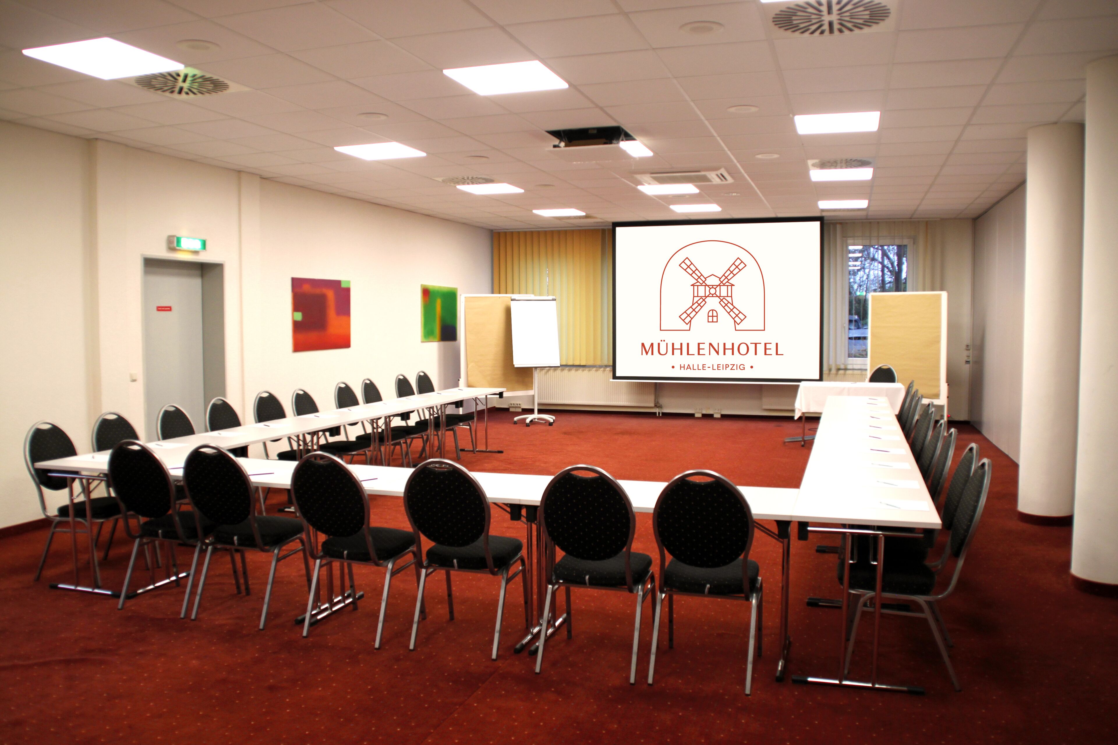 A conference room with a long table, chairs, a projector screen, and a presentation on the wall.