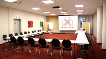 A conference room with a long table, chairs, a projector screen, and a presentation on the wall.