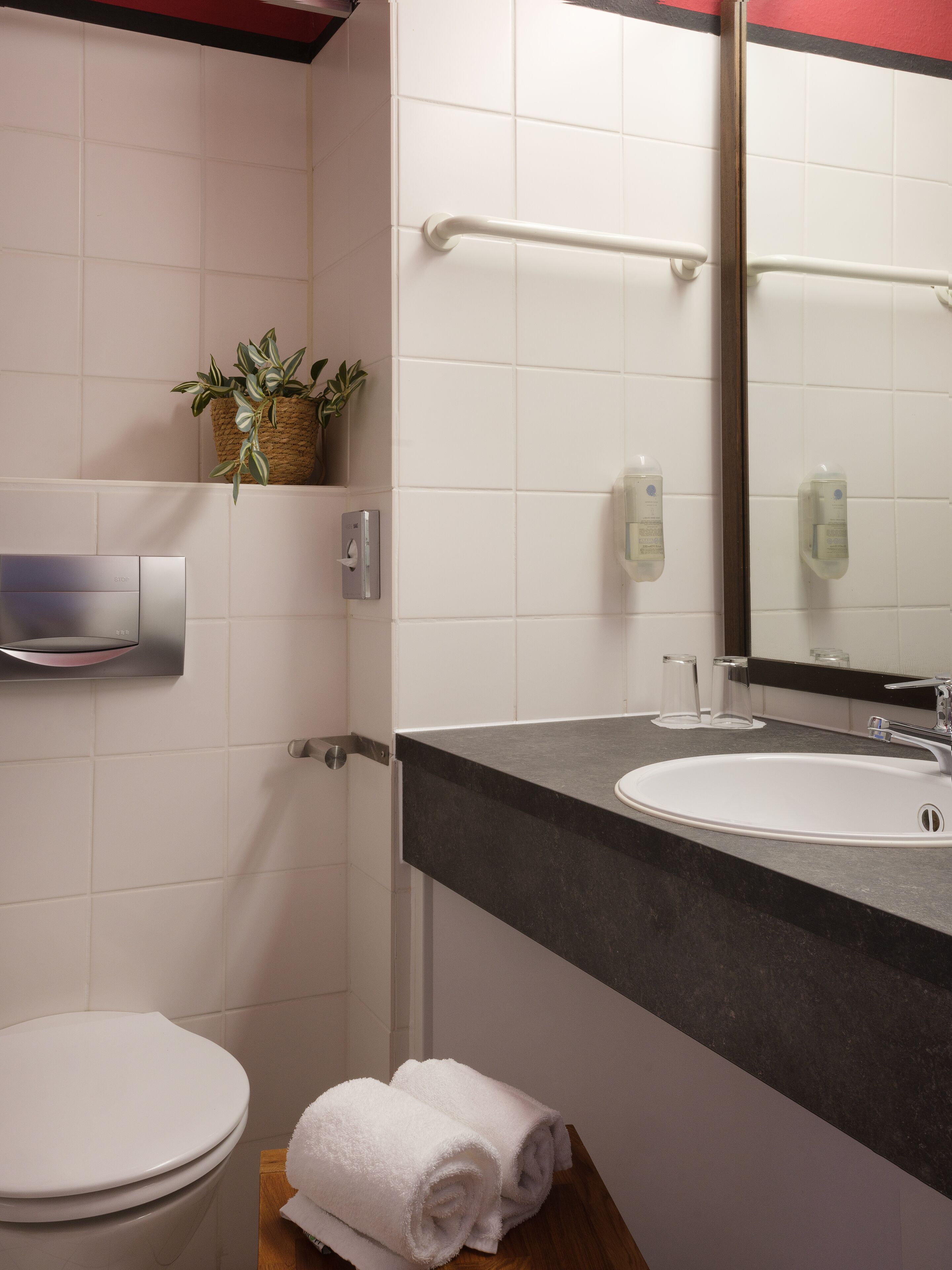 Een moderne badkamer met een wit toilet, een wastafel met donker aanrecht, een handdoekhouder en een spiegel.