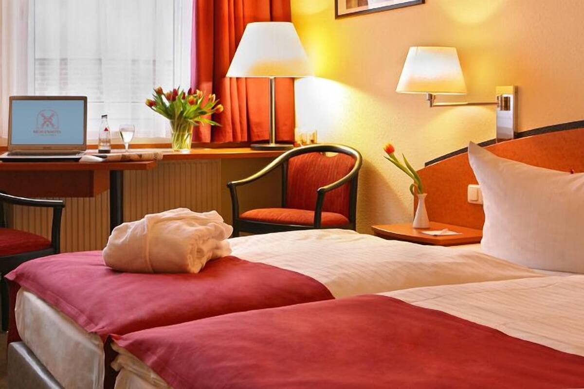 Une chambre d’hôtel avec un lit, un bureau avec un ordinateur portable, une chaise et une table de chevet avec une lampe.