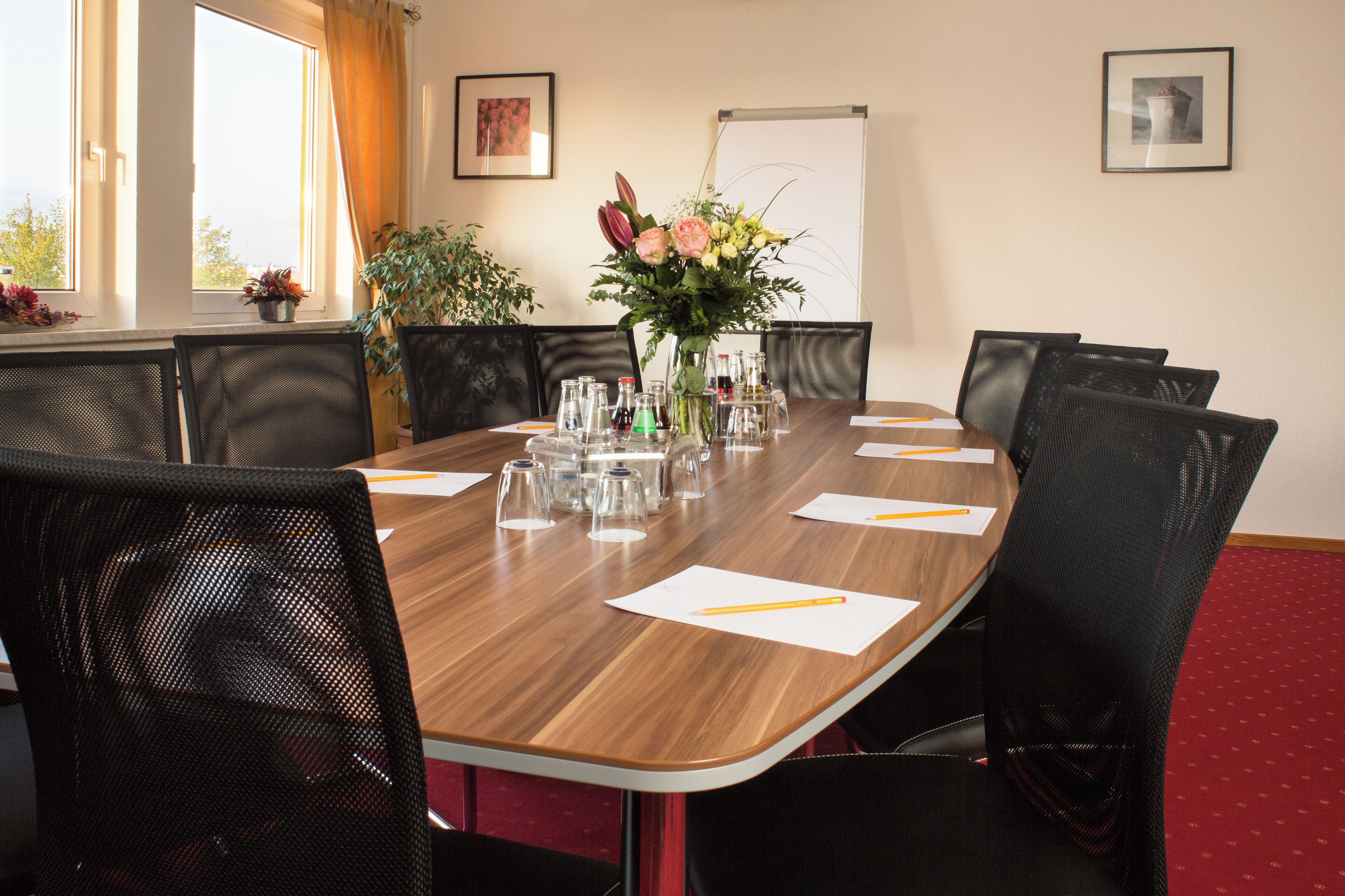 Un salón de conferencias con una mesa de madera, sillas, un jarrón de flores y una pizarra.