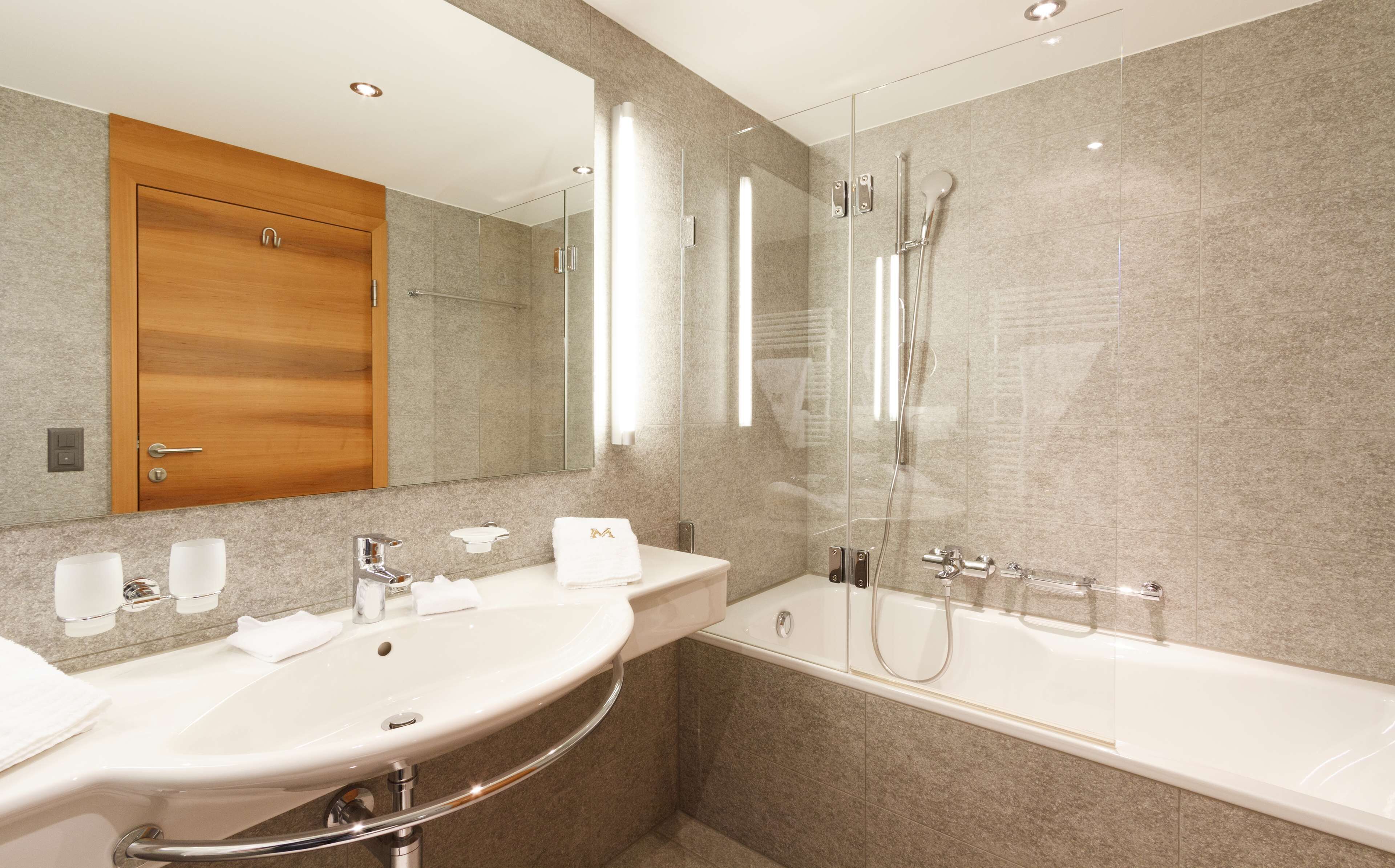 A modern bathroom with two sinks, a glass-enclosed shower, and a wooden door.
