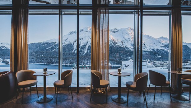 A cozy interior with large windows offering a view of snow-covered mountains and a lake. - Art Boutique Hotel Monopol (St. Moritz)