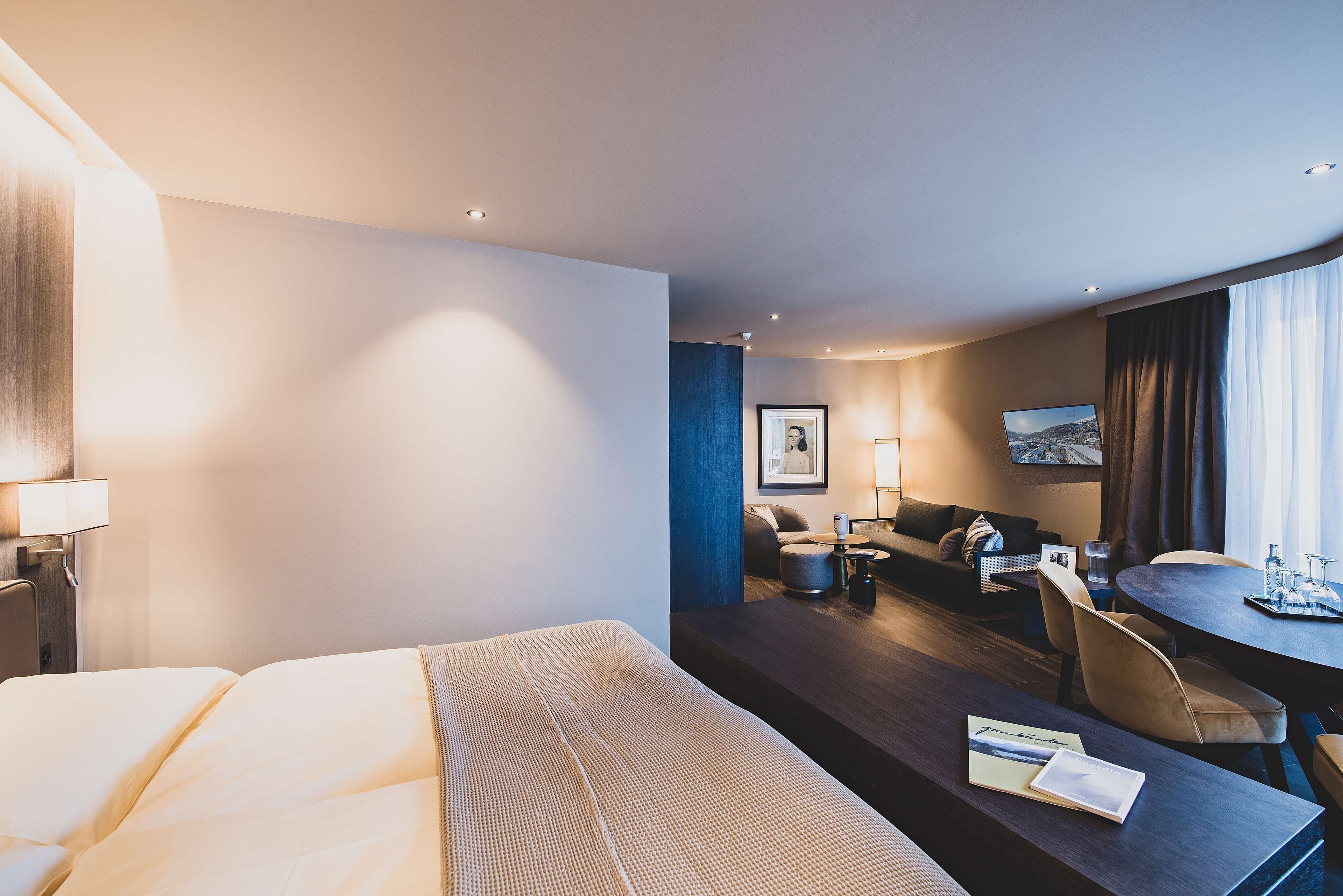 A modern hotel room with a large bed, a desk, a sofa, and a dining table.