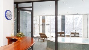 A modern hotel lobby with a wooden reception desk, a wall-mounted clock, and a large window overlooking a pool area. - Art Boutique Hotel Monopol (St. Moritz)