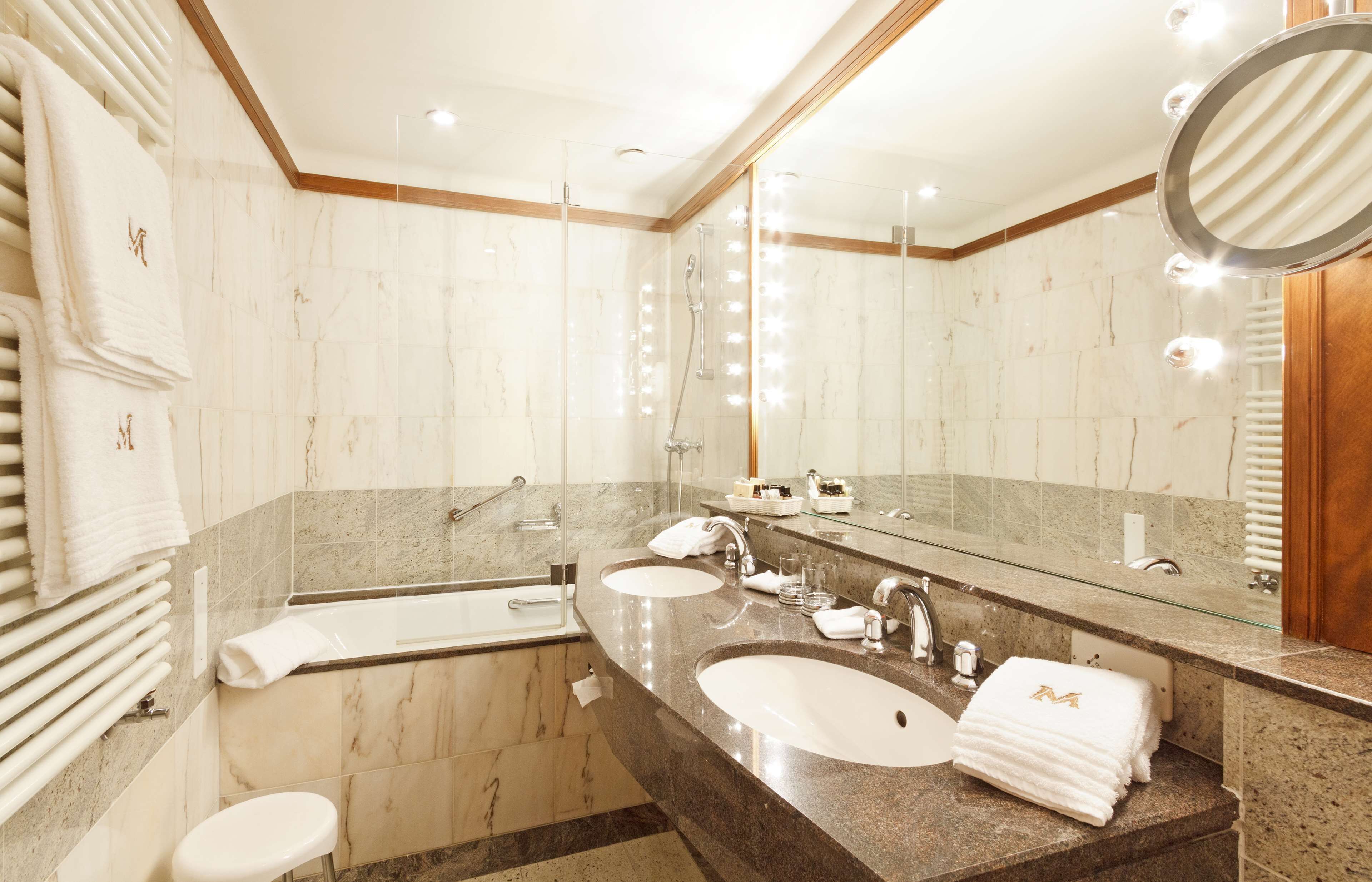 A modern bathroom with a large mirror, two sinks, a bathtub, and a toilet.