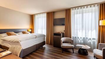 Una habitación de hotel con una cama grande, dos sillones, una mesita, un televisor y un escritorio con lámpara.
