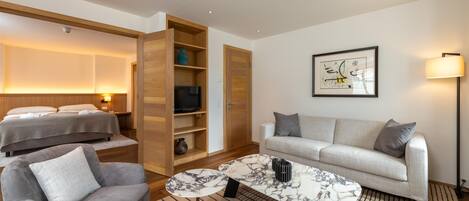 A modern hotel room with a bed, sofa, armchair, and a marble coffee table.