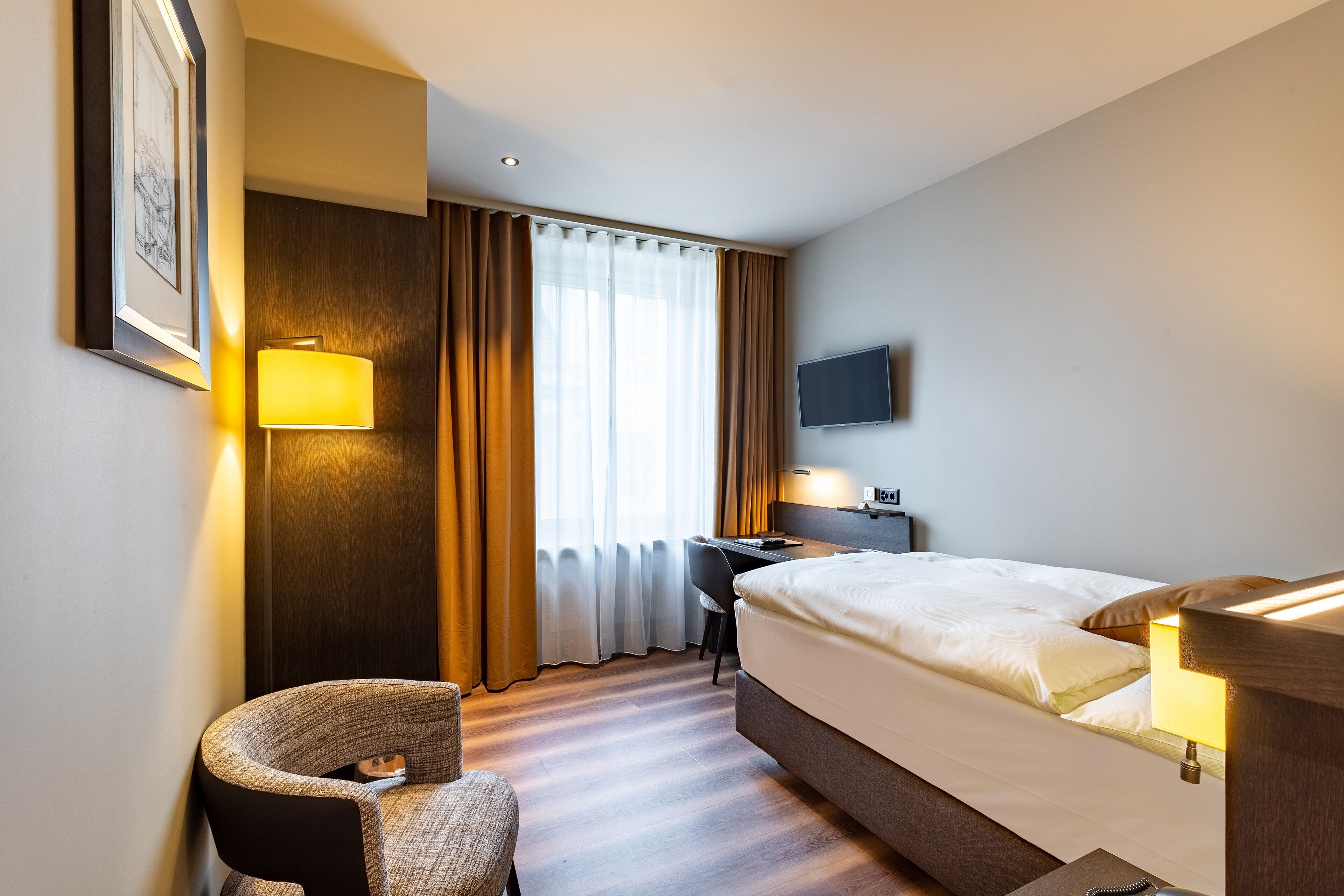 A hotel room with a bed, desk, chair, TV, and a window with curtains.