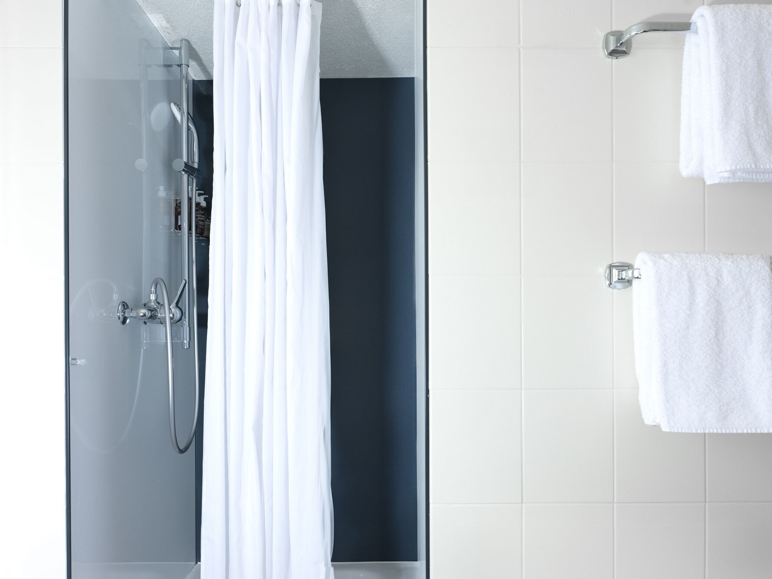 A modern bathroom with a glass shower enclosure, white towels, and a dark accent wall.